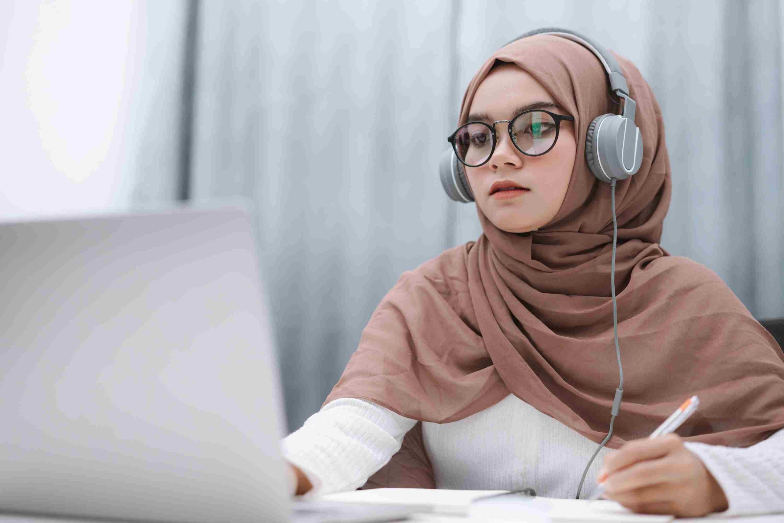 online learning - person sat at a computer with headphone completing a course or online content